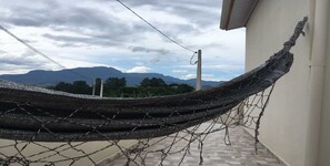 A hammock on a balcony with a view of mountains and a cloudy sky.