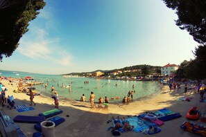 A crowded beach with people swimming and sunbathing, a clear sky, and buildings in the background. - Holiday Apartments Paloma (Pasman)