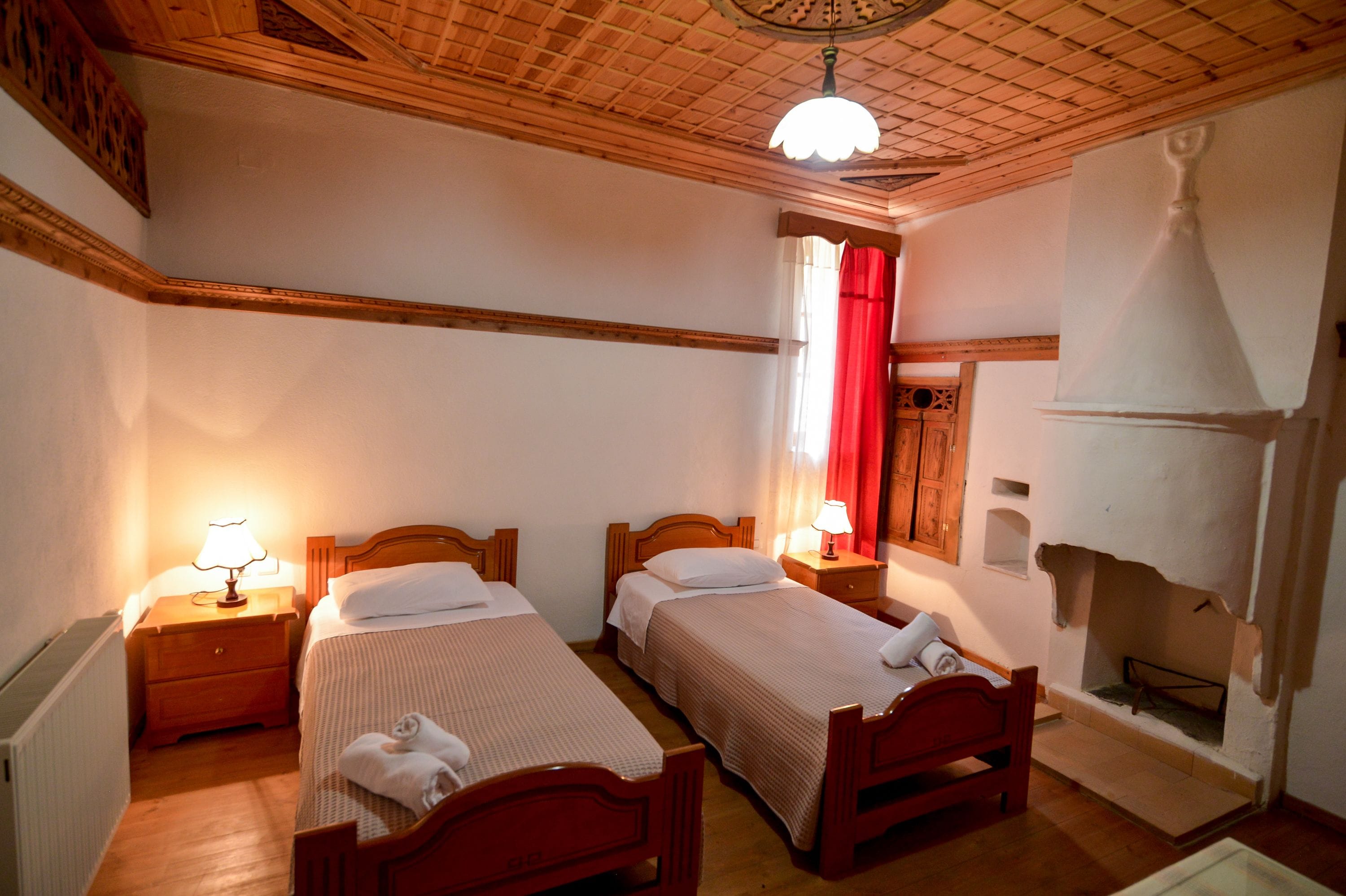 A room with two wooden beds, nightstands with lamps, a wooden ceiling, and a fireplace.