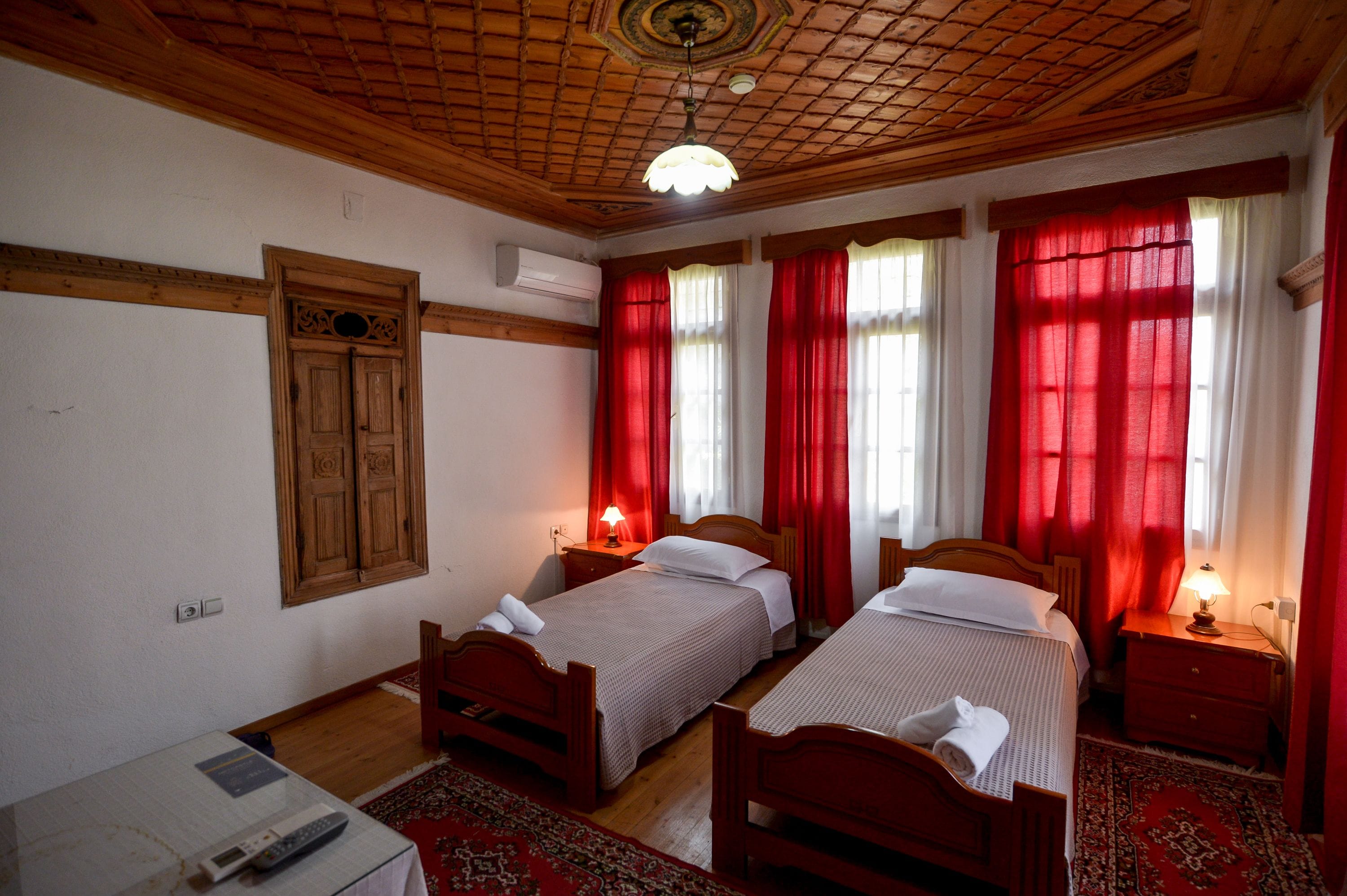 A room with two wooden beds, a wooden ceiling, and red curtains.