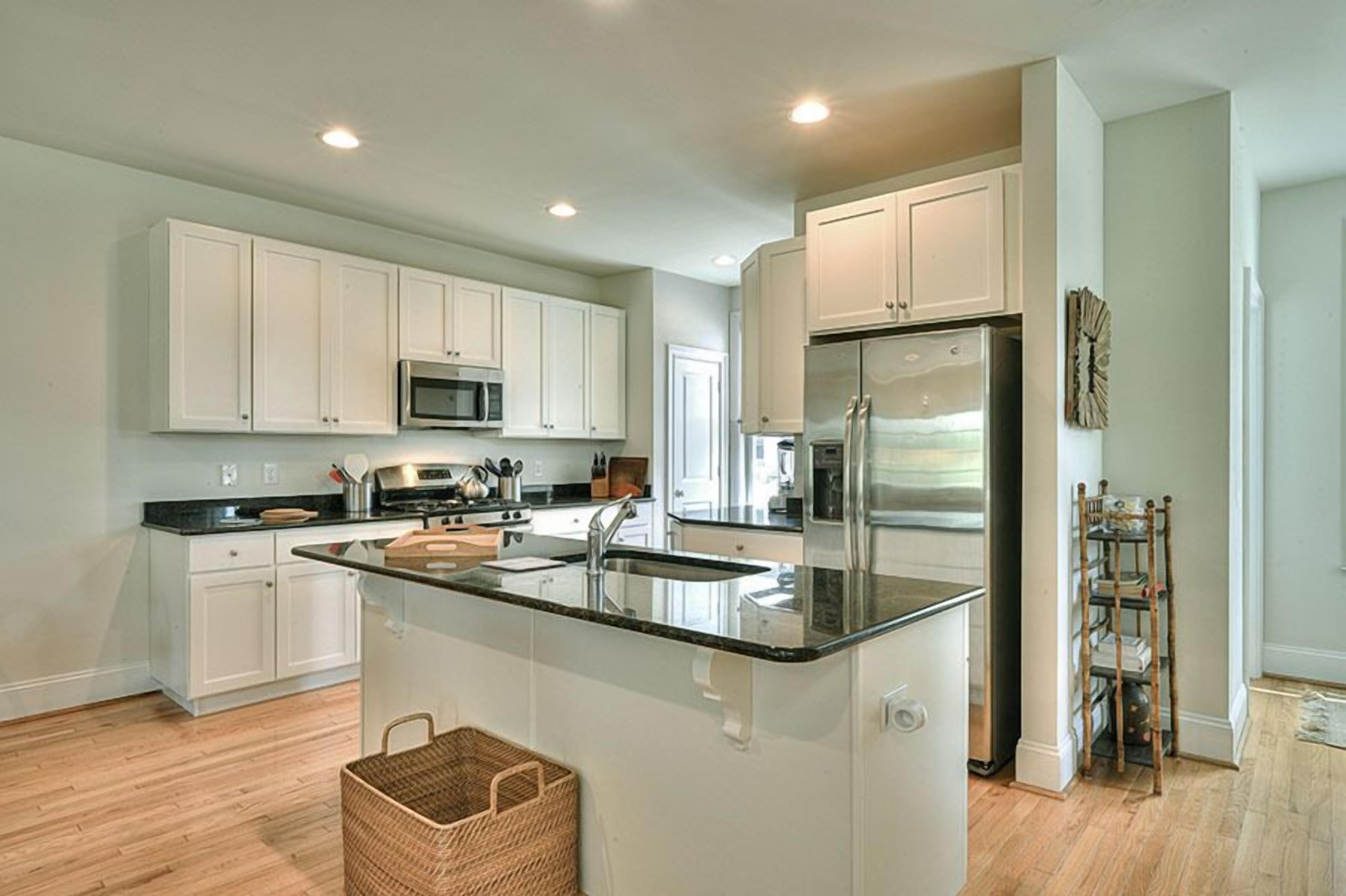 A modern kitchen with white cabinets, a central island, stainless steel appliances, and a wooden floor.