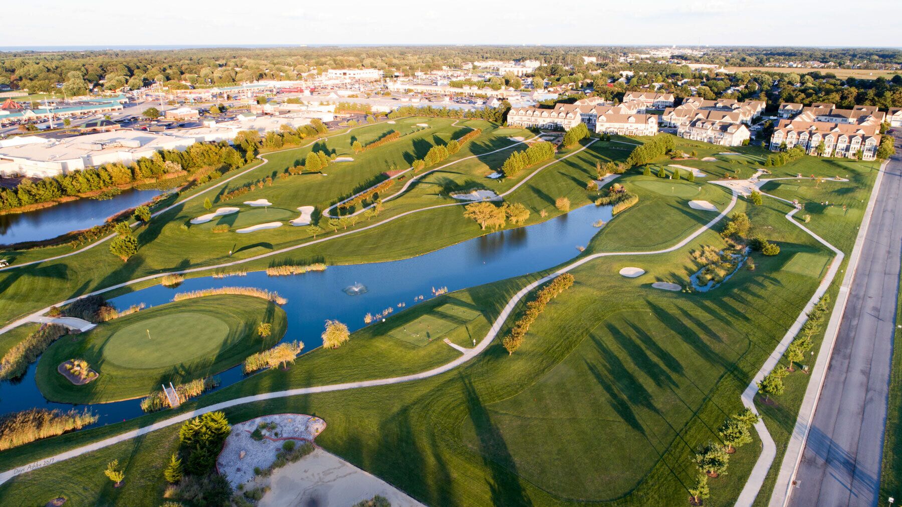 An aerial view of a golf course with a lake, surrounded by residential buildings.