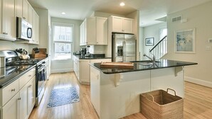 Una cocina moderna con armarios blancos, un refrigerador de acero inoxidable y una isla de encimera negra.