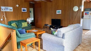 A cozy living room with wooden walls, a green sofa, a grey sofa, a wooden coffee table, and a TV stand.