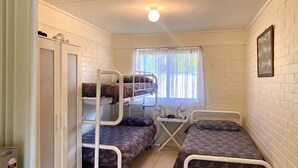 A dormitory room with bunk beds, a desk with a chair, a window with curtains, and a framed picture on the wall.