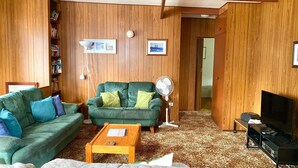 A living room with two green sofas, a wooden floor, a coffee table, a fan, and a TV stand.