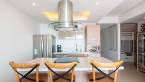 A modern kitchen with a central island, stainless steel appliances, and wooden chairs. - Spectacular Beach front 2 Bedroom Condo (Riviera Nayarit)