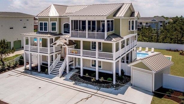 Ein mehrstöckiges Haus mit überdachter Veranda, kleinem Pool und Garage.