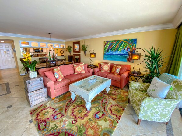 A living room with a red sofa set, a coffee table, and a patterned rug. There is a painting on the wall and a plant on the side table. - Sanibel Harbour 216: Enjoy the private beach and activities nearby-boating, kayaking, fishing! (Fort Myers)