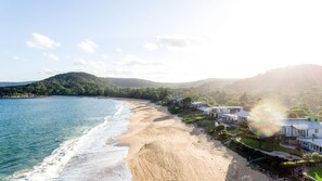 A coastal property with a beachfront, a pool, and a view of the sea and hills.
