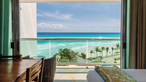 A balcony with a view of the ocean and beach, a wooden table, and a bed with a patterned pillow. - Beachfront resort in best location, walk to best clubs and restaurants (Cancún)