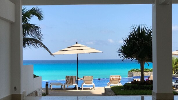 A poolside area with lounge chairs and an umbrella, overlooking a clear blue ocean. - Beachfront resort in best location, walk to best clubs and restaurants (Cancún)