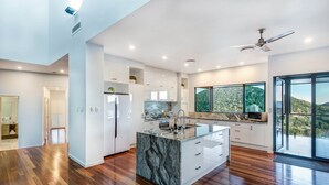 A modern kitchen with a marble island, white cabinetry, and a large window offering a view of the outdoors.