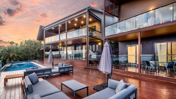 A modern house with a pool, outdoor seating, and a large glass balcony.