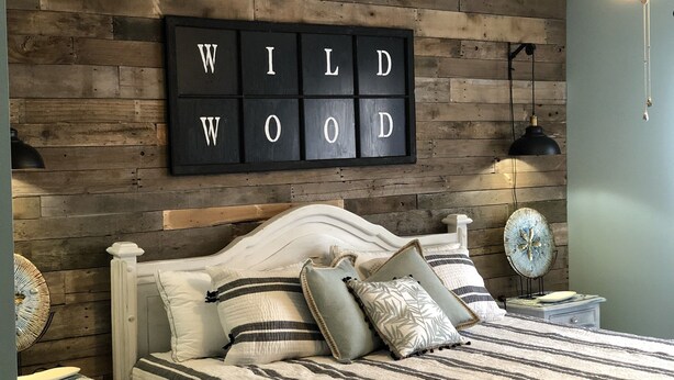 Una camera da letto con parete in legno, un letto con lenzuola a righe e un cartello 'WILD WOOD' sopra il letto.