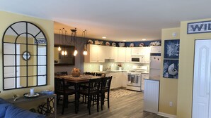 Una cucina moderna con mobili bianchi, un'area pranzo con tavolo e sedie in legno e un divano blu nella zona living.