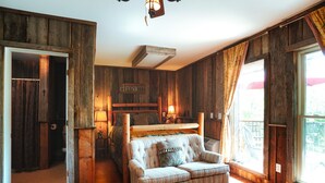 A rustic bedroom with wooden walls, a bed, a sofa, and a large window. - Tree Fort Balcony Suite (Springfield)