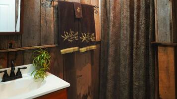 A bathroom with a wooden wall, a white sink, a plant, and a leopard print shower curtain.