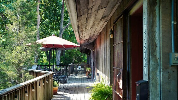 A wooden deck with outdoor seating, a red umbrella, and a sign that reads "TREASURE". - Tree Fort Balcony Suite (Springfield)