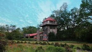 A rustic wooden tower with a red roof, surrounded by lush greenery and a field of red poppies. - Tree Fort Balcony Suite (Springfield)