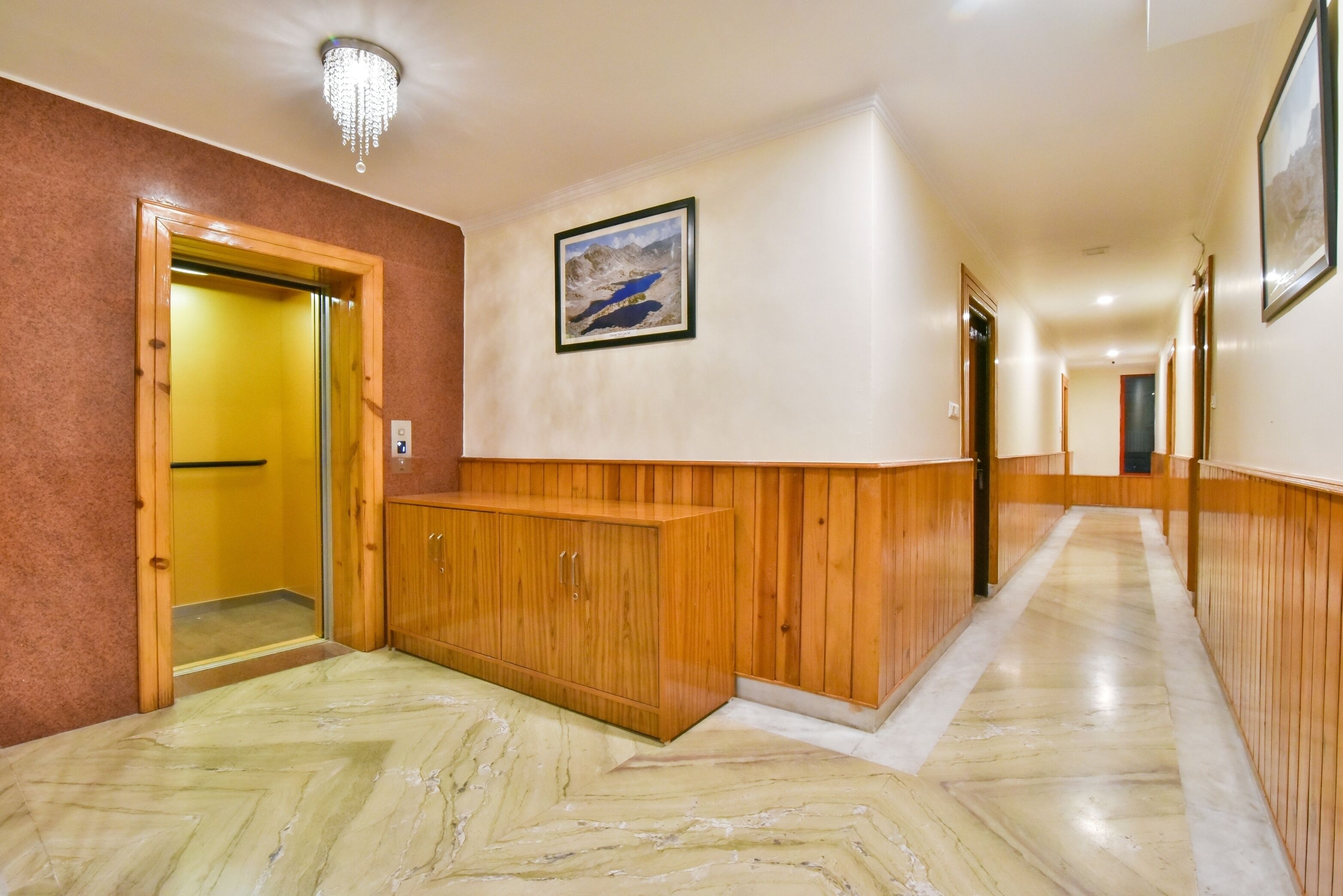 Een hotelgang met houten lambrisering, een marmeren vloer, een lijst met een afbeelding aan de muur en een deur naar een kamer.