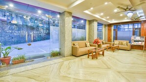 A hotel lobby with a marble floor, two sofas with patterned cushions, a coffee table, and a reception desk with brochures. -  The Posh Hotel near Mall Road with Hassle Free Covered Parking (Dharamshala)