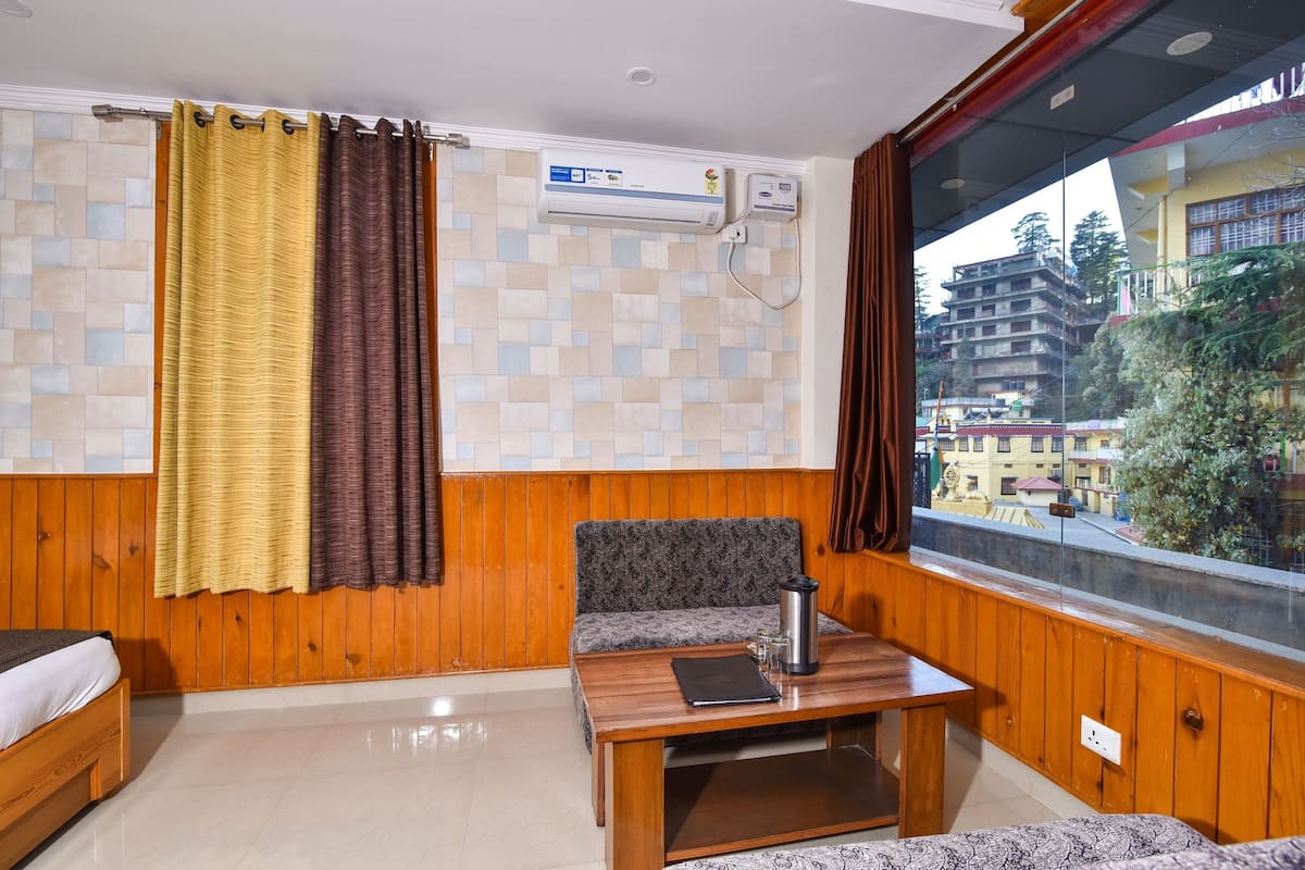 A room with a wooden bench, a table with a laptop and a thermos, and a window with a view of buildings.