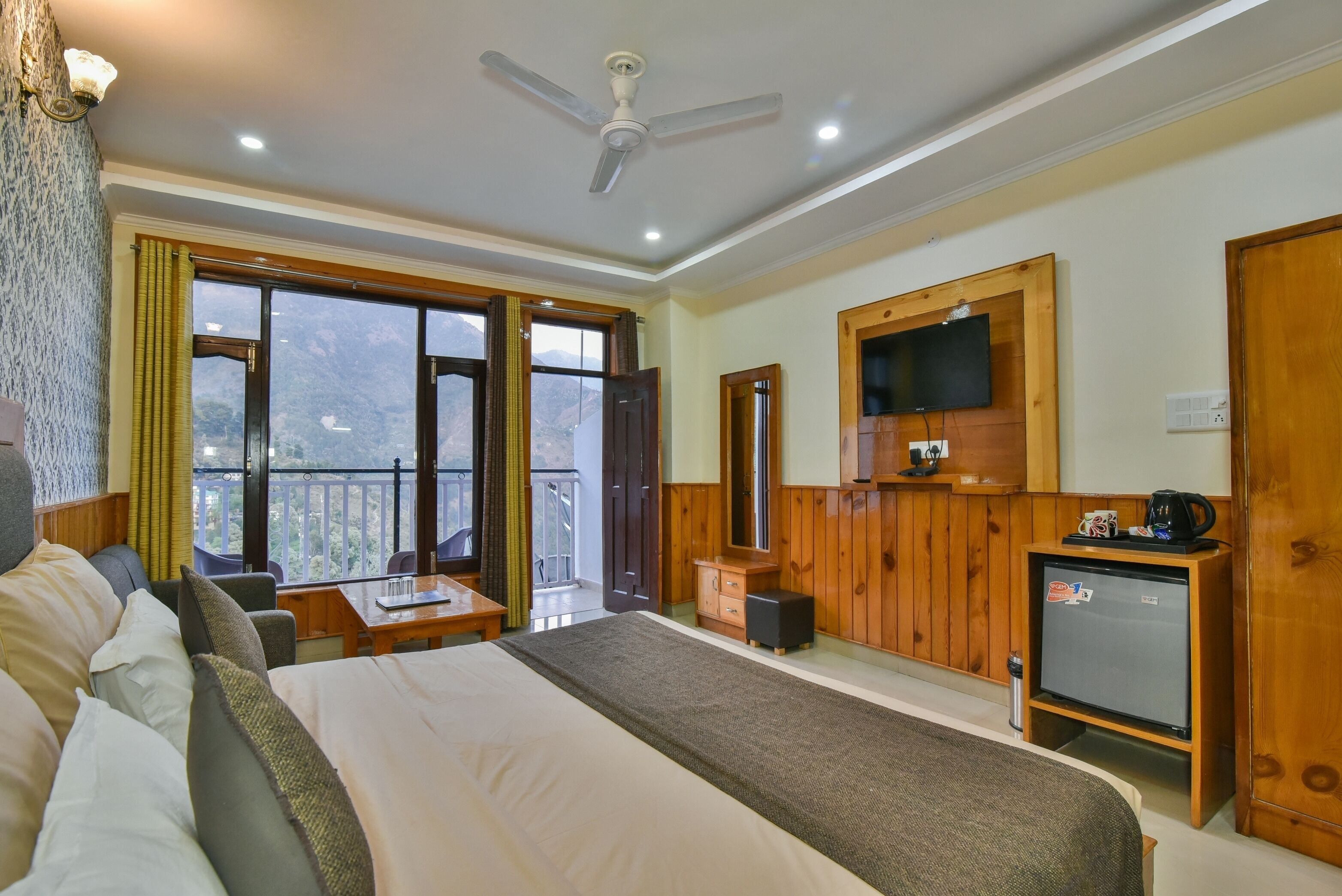 Ein Hotelzimmer mit einem großen Bett, einem Schreibtisch, einem Fernseher und einem Balkon mit Bergblick.