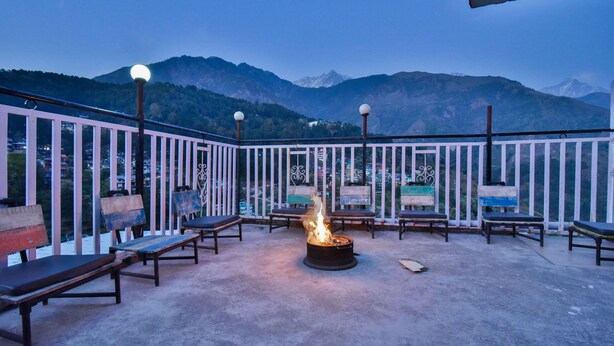 A terrace with a fire pit, benches, and a view of mountains. -  The Posh Hotel near Mall Road with Hassle Free Covered Parking (Dharamshala)