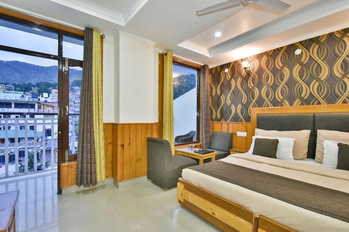 A hotel room with a large bed, a desk, a chair, and a view of a cityscape through large windows.