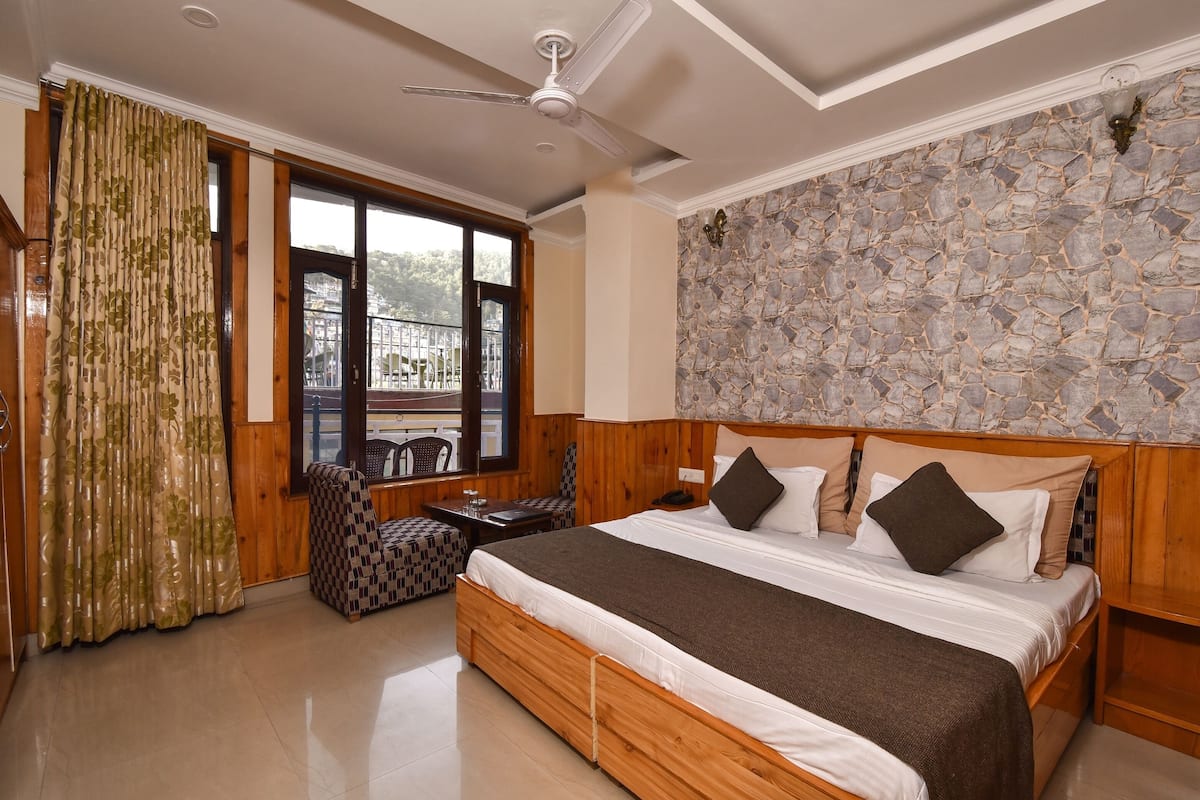 A bedroom with a large bed, wooden headboard, stone wall, and a view through a window.