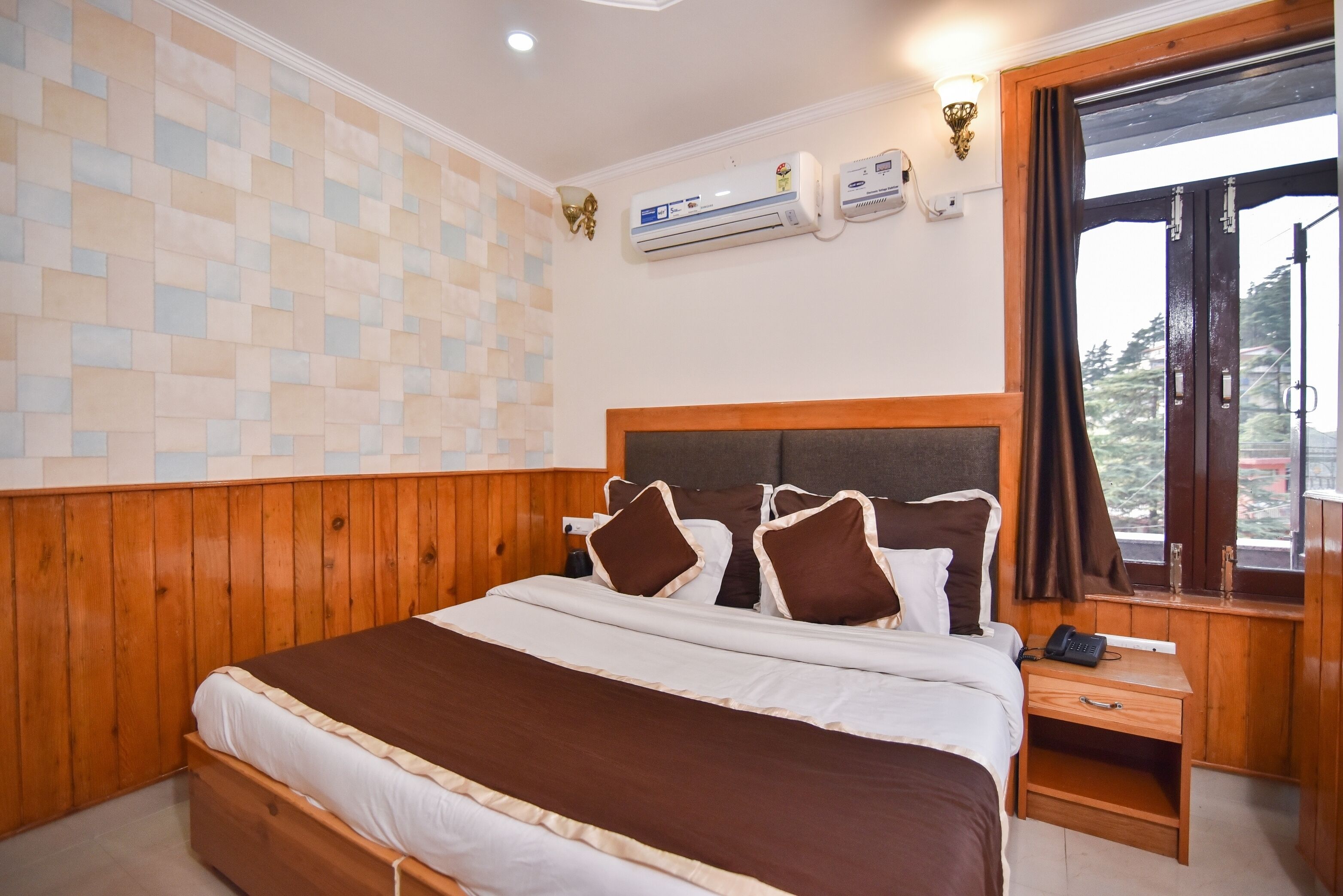A bedroom with a wooden headboard, a large bed with brown and white bedding, an air conditioning unit, a bedside table with a phone, and a window with curtains.