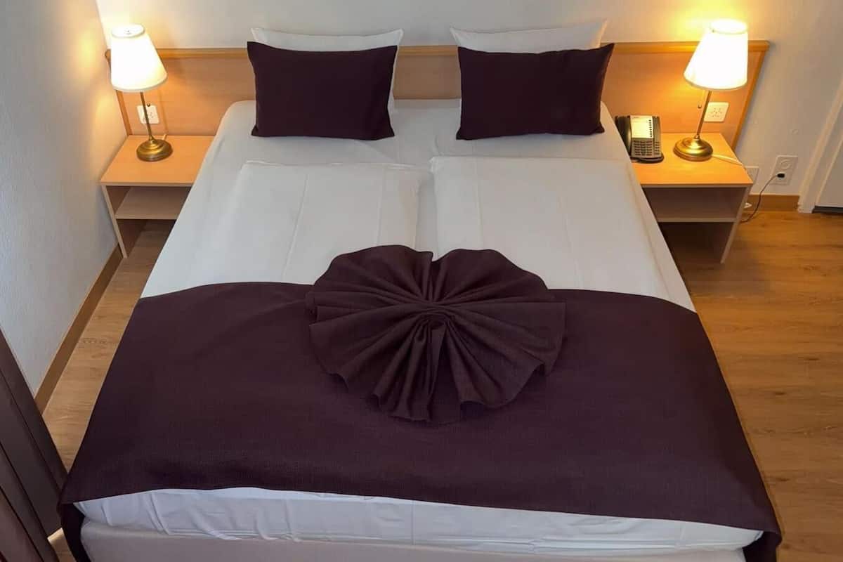 A double bed with white linens and a large decorative pillow. There are two bedside tables with lamps and a phone.