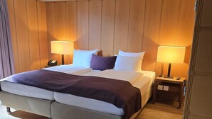A large bed with a wooden headboard, two bedside tables with lamps, and a wooden floor. - Hotel Olympia (Zürich)