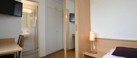 Quarto de hotel com cama, escrivaninha, espelho, televisão e guarda-roupa.