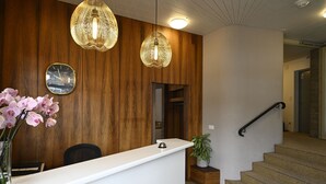 A reception area with a wooden wall, a white reception desk, a clock, and a staircase. - Hotel Olympia (Zürich)