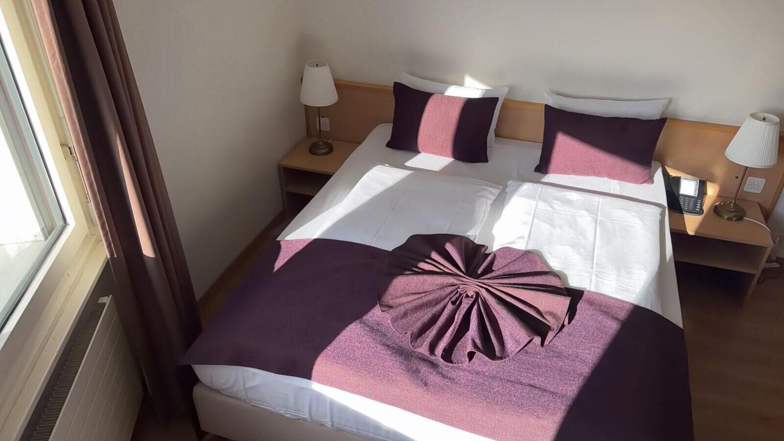 Quarto de hotel com uma cama, duas mesinhas de cabeceira, uma janela com cortinas e uma luminária em cada mesa.