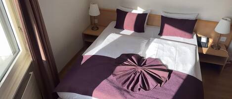 Quarto de hotel com uma cama, duas mesinhas de cabeceira, uma janela com cortinas e uma luminária em cada mesa.