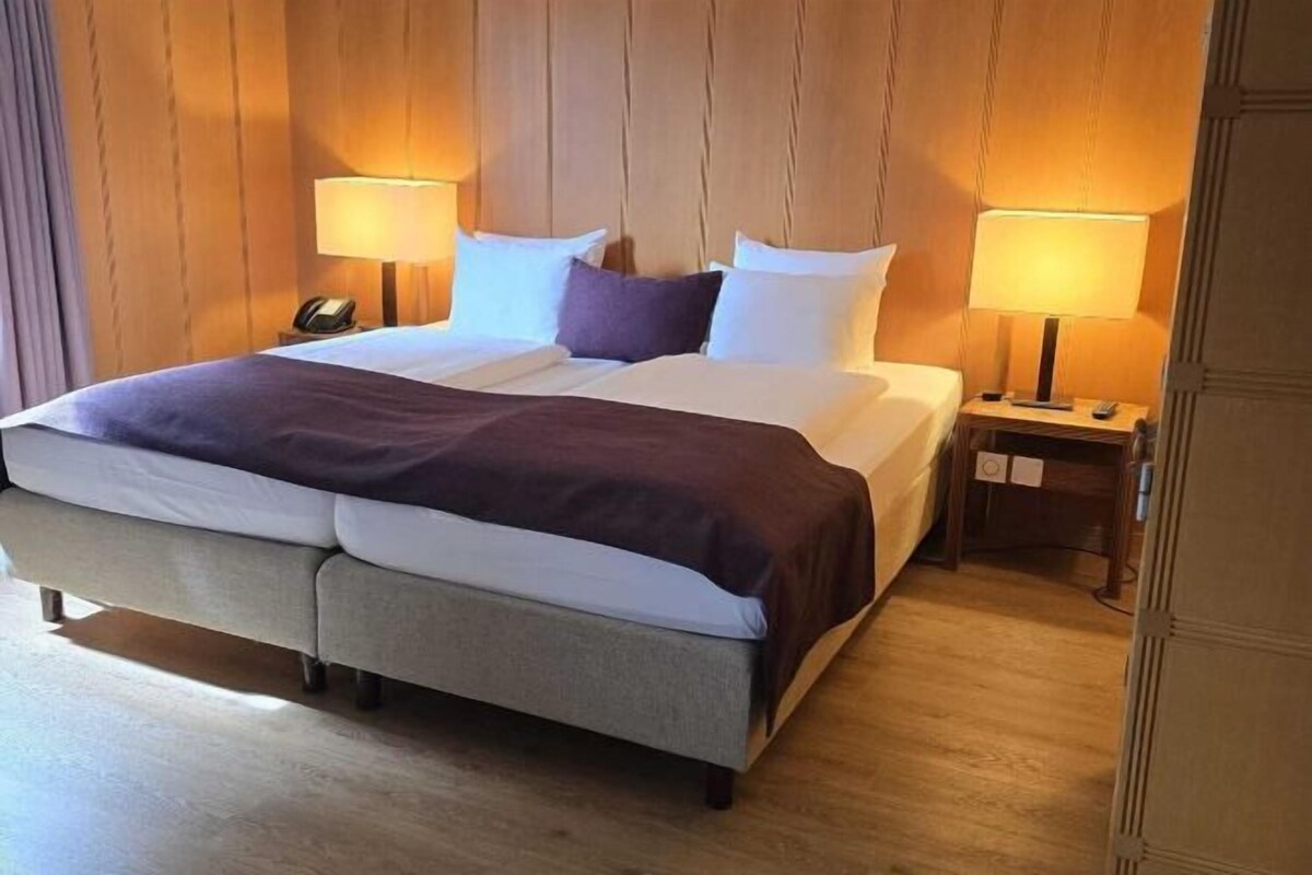 A hotel room with a large bed, two bedside tables with lamps, and a wooden wall paneling.