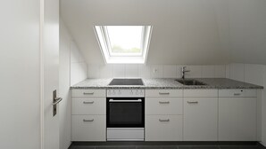 A modern kitchen with white cabinets, a granite countertop, a built-in oven, and a skylight. - Hotel Olympia (Zürich)