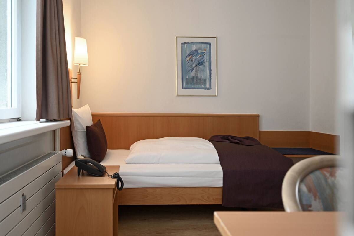 A hotel room with a bed, bedside table, lamp, and a framed artwork on the wall.