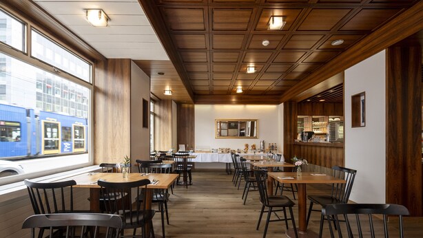 A restaurant with wooden tables and chairs, a kitchen in the background, and a view of a train outside. - Hotel Olympia (Zürich)