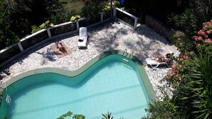 Una piscina con cubierta de piedra, rodeada de abundante vegetación y una valla blanca.