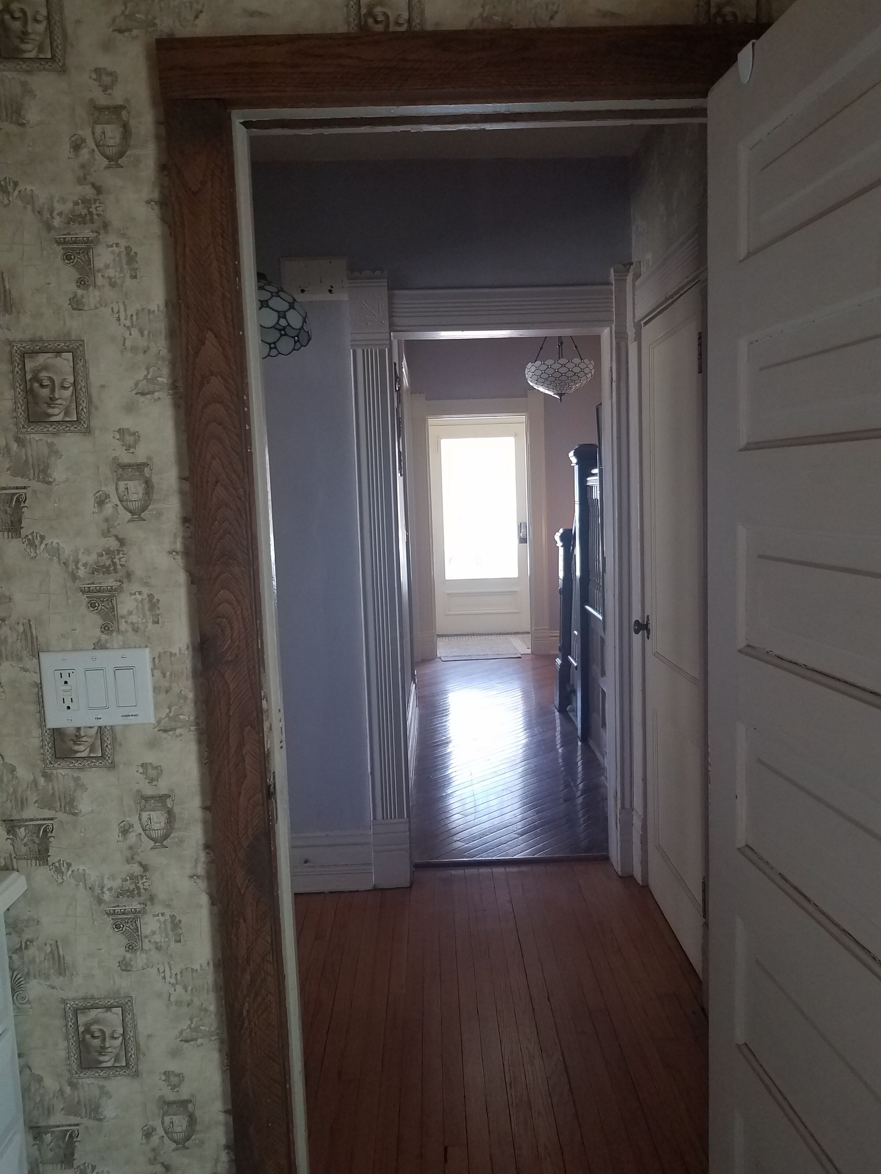 A hallway with wooden flooring, a door on the right, and a window at the end.
