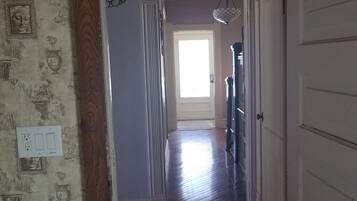 A hallway with wooden flooring, a door on the right, and a window at the end.