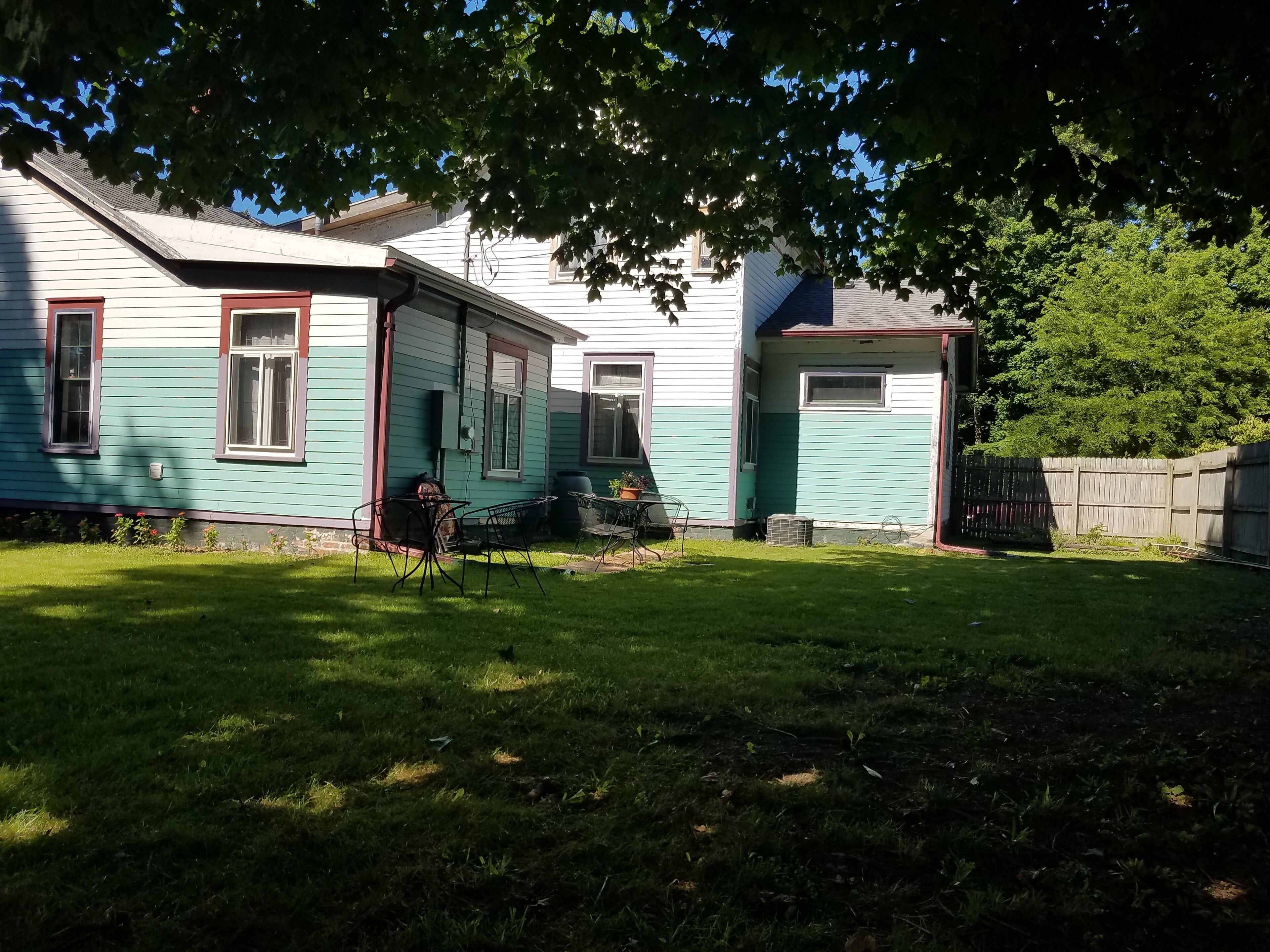 Ein Haus mit Vorgarten, einer Terrasse mit Stühlen und einem kleinen Tisch.