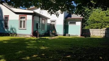 Ein Haus mit Vorgarten, einer Terrasse mit Stühlen und einem kleinen Tisch.