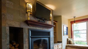 Una chimenea de piedra con un televisor encima, un banco de madera con cojines, y una alfombra roja.