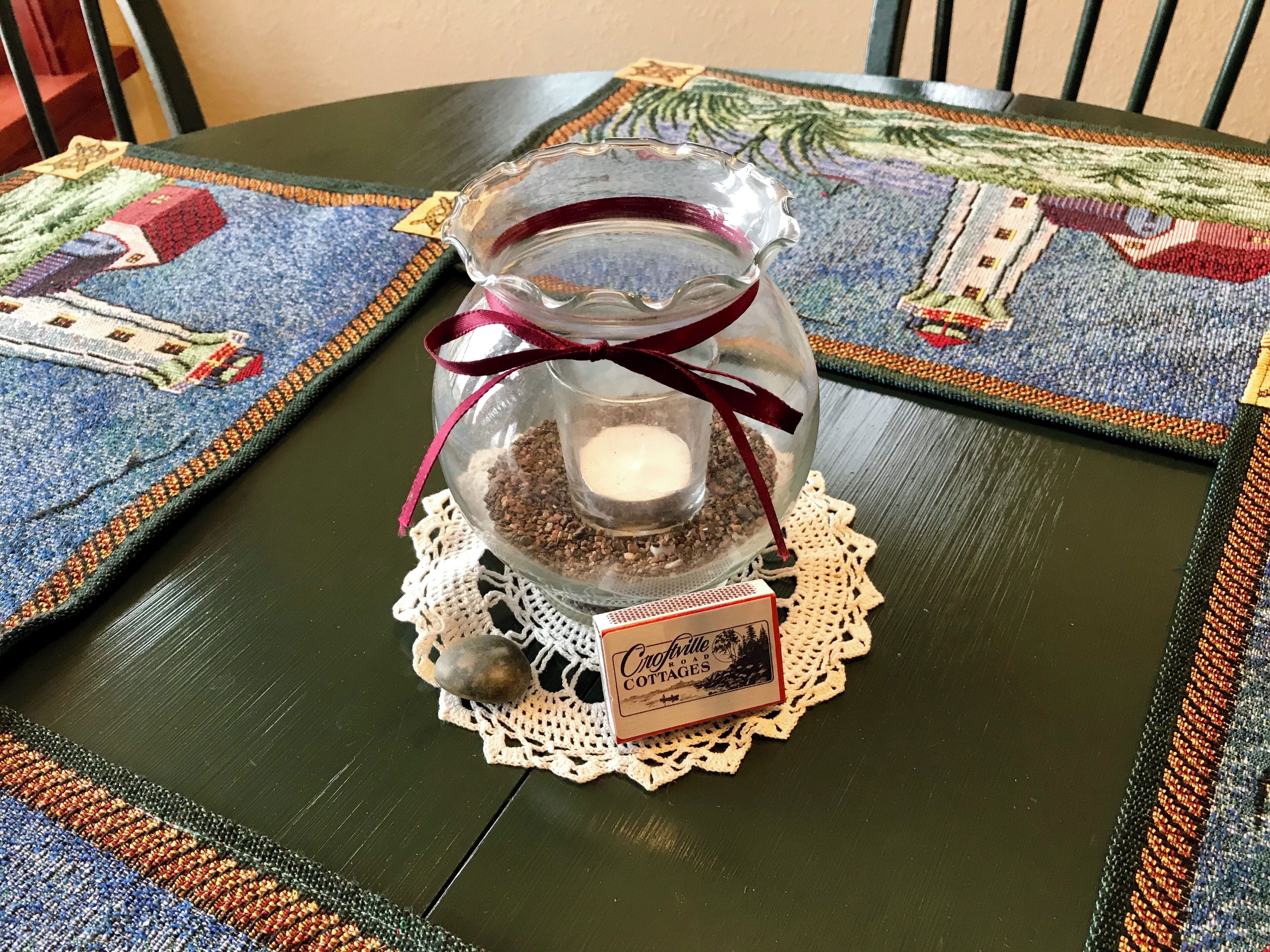 A glass jar with a candle and a doily on a table with a patterned tablecloth.