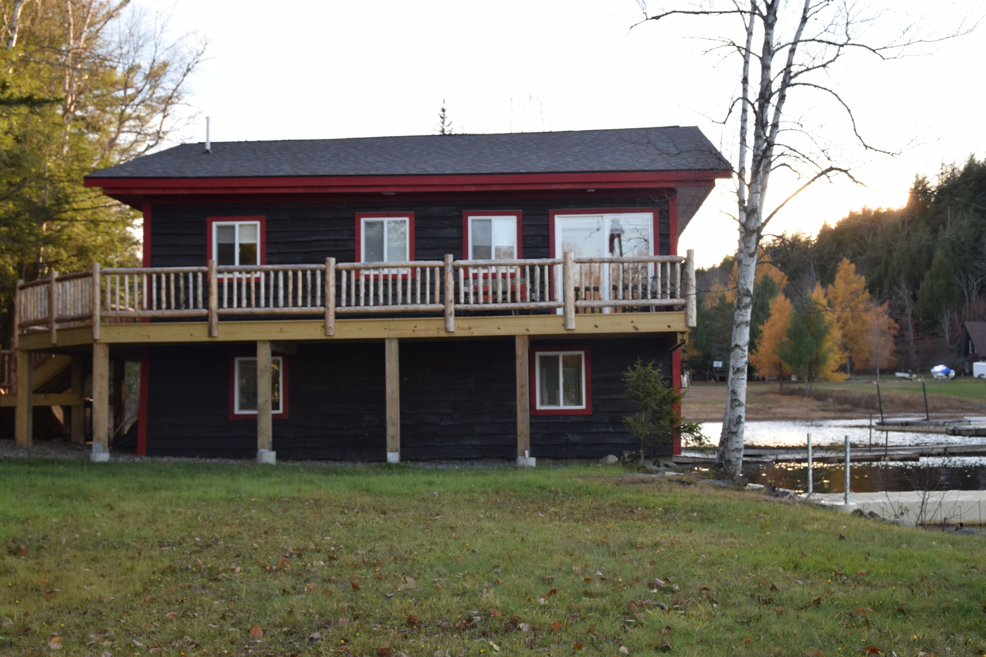 A two-story log cabin with a balcony, a small porch, and a pond in the background.